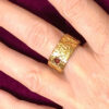 Bague semi-ouverte large en laiton réticulé avec un grenat incrusté sur le côté portée sur le majeur gauche d'une femme qui porte une veste velours fuchsia dont on ne voit que la main