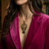 pendentif composé d'engrenages et d'un papillon en alliage orné d'un péridot vert et perle oeil de tigre vert montée sur axe et avec une bélière couleur bronze porté sur une chaine courte dorée par une femme brune aux cheveux longs dont one ne voit que le buste et le bas du visage, et qui porte une veste en velours rose fuchsia