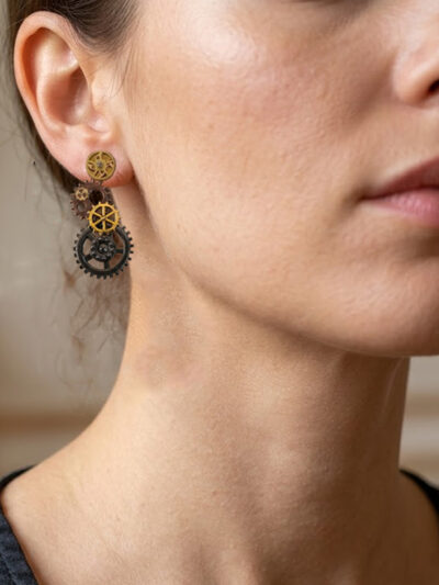 Boucles d'Oreilles composées de 5 engrenages collés verticalement portée sur l'oreille droite d'une femme brune au cheveu long attachés dont on ne voit que le bas du visage