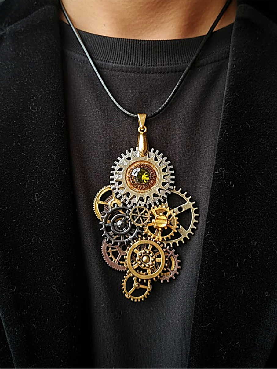 pendentif composé d'engrenages en alliage orné d'un péridot vert et avec une bélière dorée porté sur un cordon de cuir marron foncé par un homme don ton ne voit que le buste et qui porte un tee-shirt et une veste ouverte noire