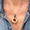 recto du pendentif en laiton fondu et formé en pépites avec un cabochon de verre rouge au centre. porté par une femme avec une chemise en jean bleue ouverte.