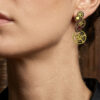 Boucles d'Oreilles composées de 5 engrenages collés verticalement avec un grenat sur chaque boucle portée sur l'oreille gauche d'une femme brune au cheveu long attachés dont on ne voit que le bas du visage