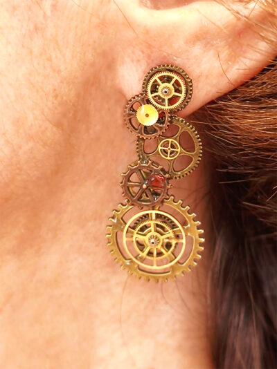 Boucles d'Oreilles composées de 5 engrenages collés verticalement avec un grenat sur chaque boucle portées sur l'oreille gauche par une femme rousse dont on ne voit que l'oreille et le bas du visage