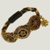 Bracelet en paracorde tressée avec des engrenages couleur bronze dessus consolidé par fil de laiton dessous et un fermoir noir magnétique à l'arrière, Bracelet en paracorde tressée avec des engrenages couleur bronze dessus et fil de laiton dessous porté par un homme brun barbu dont on ne voit que le poignet et le bas du visage, style steampunk
