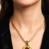 pendentif en laiton fondu et formé en pépites avec un cabochon de verre rouge au centre porté avec une chaine doublée d'un cordon par une femme ayant une chemise noire ouverte, style chic bohème