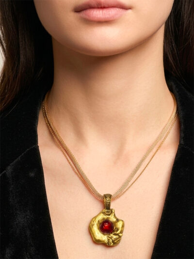 pendentif en laiton fondu et formé en pépites avec un cabochon de verre rouge au centre porté avec une chaine doublée d'un cordon par une femme ayant une chemise noire ouverte, style chic bohème