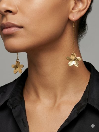 Boucles d'oreilles pendantes en forme de petites fleurs en laiton martelé attachées à des crochets dorés par une fine chaine dorée portées par une femme brune aux cheveux attachés dont one voit que le bas du visage et qui porte une chemise noire