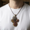 Pendentif composé d’engrenages alliage, orné de 2 Grenats et d'une Agate marron montée sur un axe avec une bélière gravée de couleur bronze porté avec un cordon court en cuir foncé par un homme dont on ne voit que le buste et qui porte un tee shirt blanc