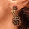 Boucles d'Oreilles composées de 5 engrenages collés verticalement portées sur l'oreille gauche par une femme rousse dont on ne voit que l'oreille et le bas du visage