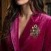 Broche engrenages coeur et étoile en alliage avec des grenats et deux perles calcédoine rose foncé montées sur un axe portée par une femme brune au cheveu long dont on ne voit que le bas du visage sur le revers de sa veste en velours rose fuchsia