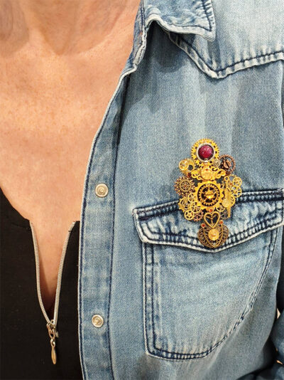 recto Broche engrenages plume en alliage avec des grenats et une perle calcédoine rose foncé portée par une femme ayant une chemise en jean et un tee shirt noir