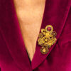 recto Broche engrenages plume en alliage avec des grenats et une perle calcédoine rose foncé porté par une femme portant une veste velours fuchsia dont on ne voit que le buste