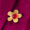 Recto d'une Broche en laiton martelé en forme de grosse fleur avec un cabochon de verre rouge au centre entourée de petites perles dorées portée sur une veste en velours rose fuchsia