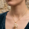 Pendentif Coquillage orné de perles dorées porté sur une chaine courte fine dorée par une femme brune aux cheveux attachés dont on ne voit que le bas du visage et le buste