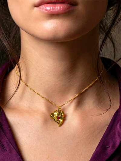 pendentif pépite laiton fondue ornée de petites perles dorées et d'une grenat avec anneau en laiton portée sur une chaine courte dorée par une femme brune aux cheveux attachés avec quelques mèches tombantes qui portent une chemise en lin violet