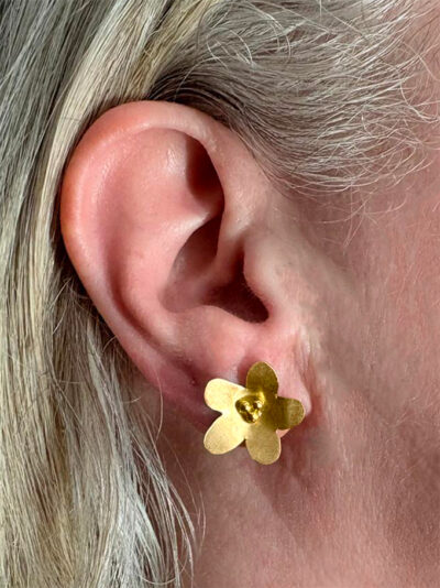 recto boucles d'oreilles clous en forme de fleur laiton doré avec 3 petites perles dorées portées sur l'oreille droite par une femme blonde dont on ne voit que l'oreille et une partie des cheveux