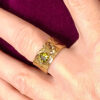 dessus de bague semi ouverte en laiton doré réticulé avec péridot vert portée par une femme au majeur gauche qui porte une veste velours fuchsia