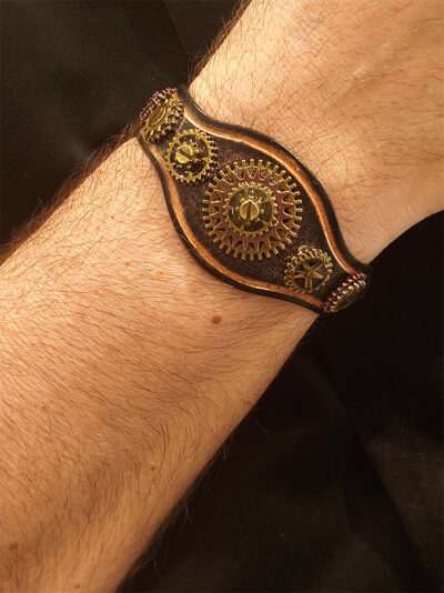 Bracelet cuir vieilli avec engrenages laiton vieilli et grenats porté par un homme avec veste noire dont on ne voit que le poignet