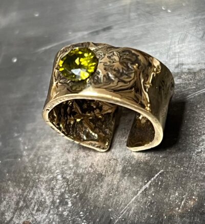 vu de dessus d'une bague anneau large en laiton doré réticulé avec une pierre verte sur le dessus au centre