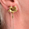 recto boucles d'oreilles en forme de fleur en laiton doré avec cabochon verre ambre au centre et en dessous pendantes 2 chaînes dorée or portée sur l'oreille droite par une femme blonde