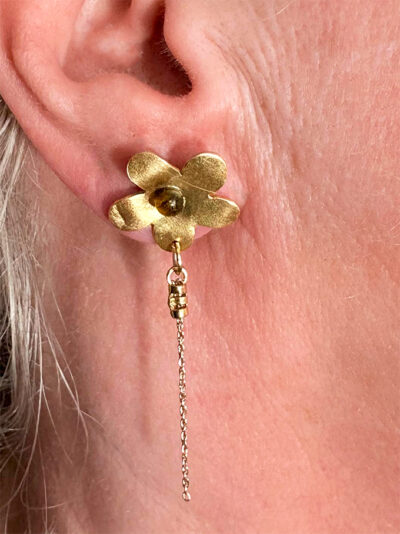 recto boucles d'oreilles en forme de fleur en laiton doré avec cabochon verre ambre au centre et en dessous pendantes 2 chaînes dorée or portée sur l'oreille droite par une femme blonde