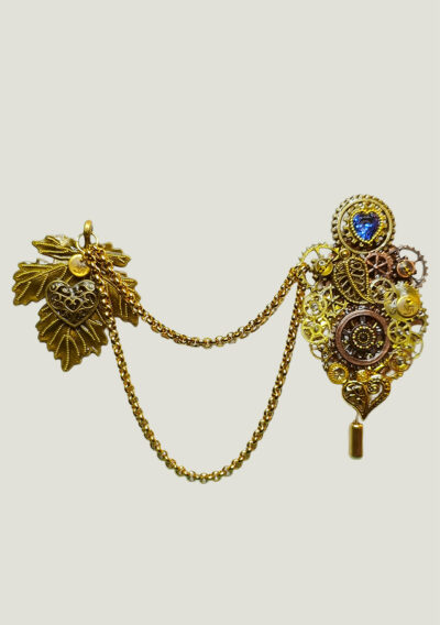 Recto Broche duo Steampunk composée d'engrenages et d'éléments divers (dont une grande feuille) en alliage de bronze reliées par une double chaîne et ornées de petites perles dorées et d'un cristal bleu véritable.