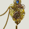 Recto Broche duo Steampunk composée d'engrenages et d'éléments divers (dont une grande feuille) en alliage de bronze reliées par une double chaîne et ornées de petites perles dorées et d'un cristal bleu véritable.